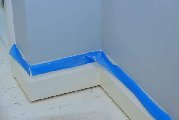 Blue painter's tape is applied along the baseboards of a home.