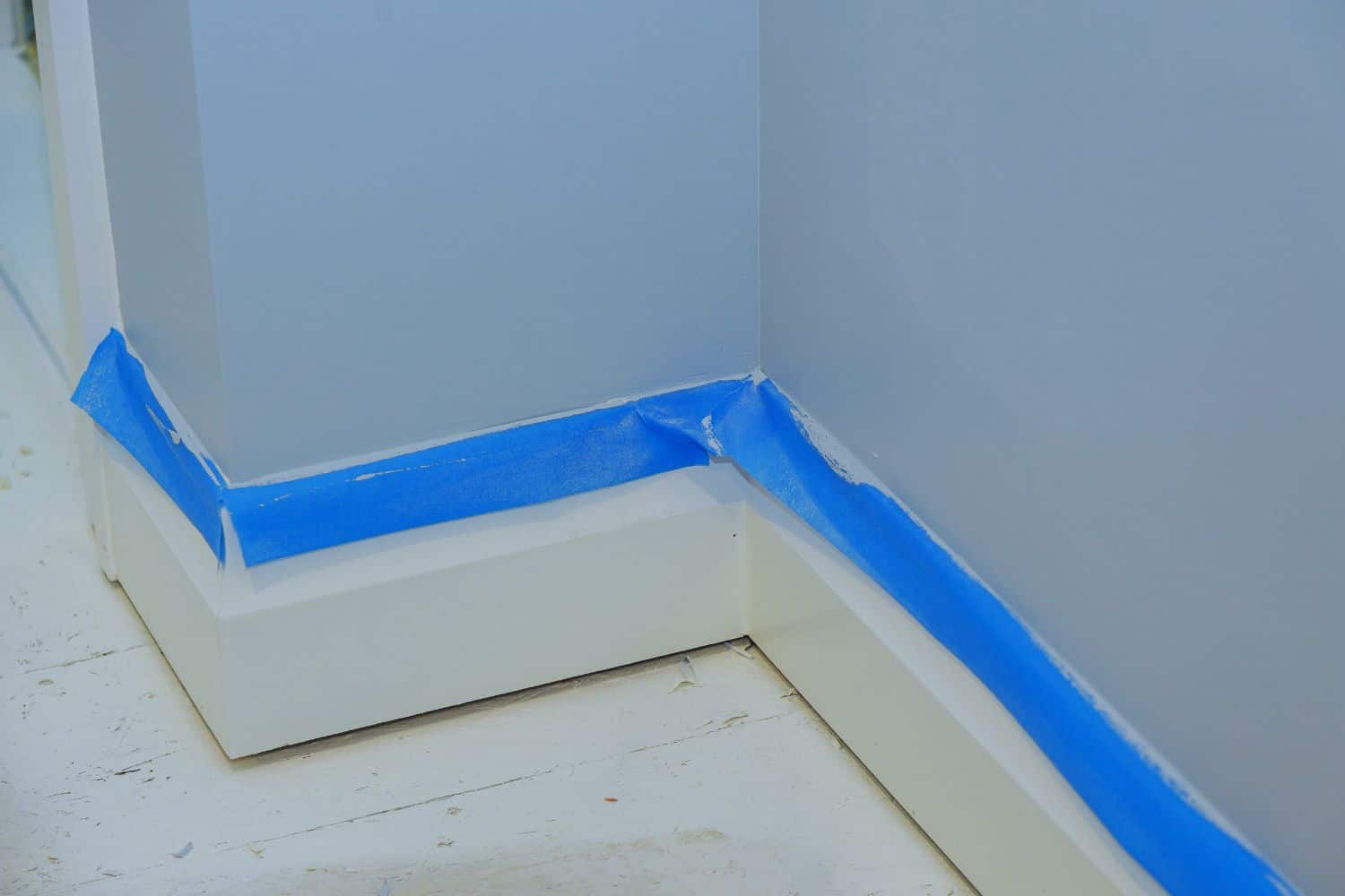 Blue painter's tape is applied along the baseboards of a home.