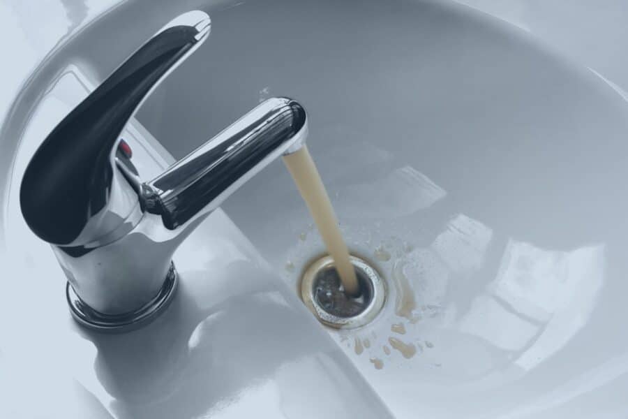 Discolored, brownish water running from a chrome faucet into a white sink basin.