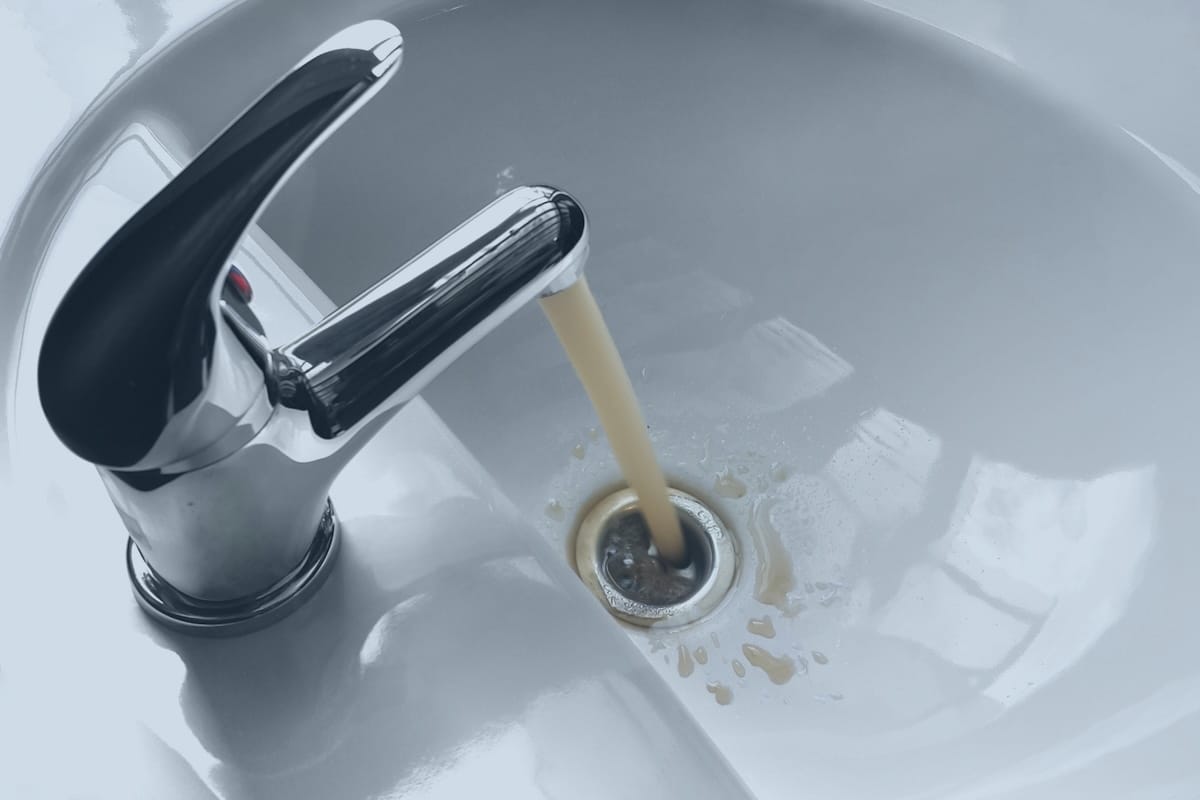 Discolored, brownish water running from a chrome faucet into a white sink basin.
