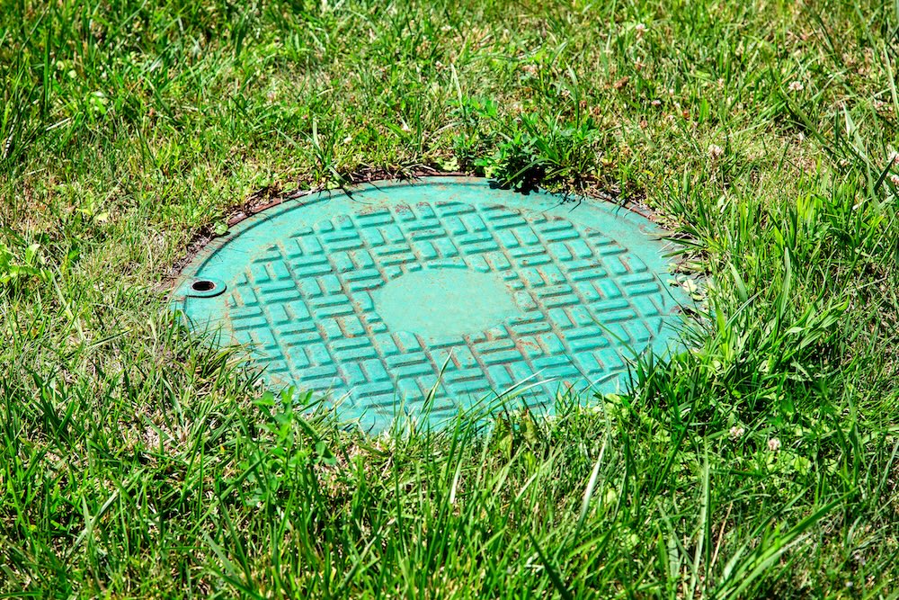 A round green plastic septic tank cover sits flush with the ground in a grassy lawn.