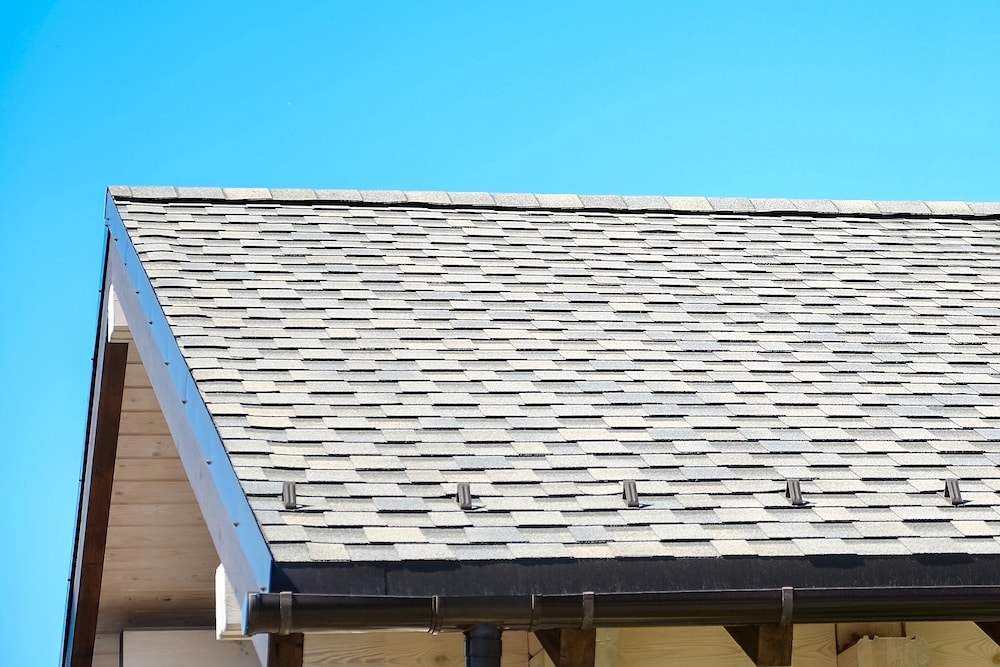 Low-angle exterior view of a shingled roof with a low-profile ridge vent installed along the top peak against a blue sky.