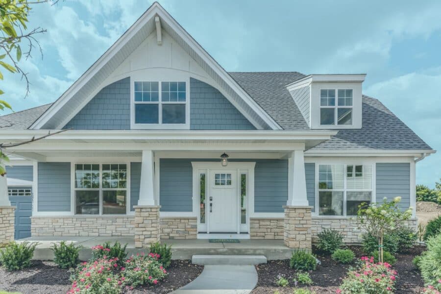 A charming blue Craftsman-style home featuring a spacious front porch with stone-based columns and neatly manicured landscaping.